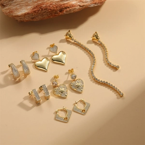 Golden heart and star dangle earring set with shimmering zircons on a beige background