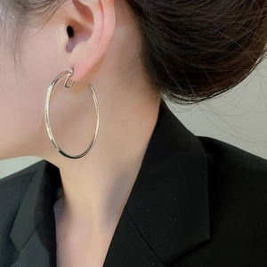 Close-up of a large minimalist silver hoop earring worn by a model in a black suit
