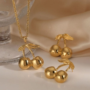 Golden cherry necklace and earrings jewelry set displayed on elegant glass and beige silk