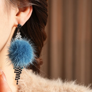Close-up of diamond-studded rhombic earrings with blue pompom tassels and silver needles
