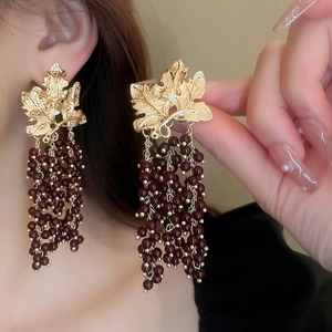 Detail of vintage gold maple leaf earrings with dark red beaded tassels on a model