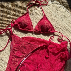 Detail of rose red lace bikini set with matching mesh skirt on straw background