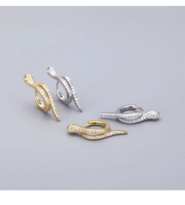 Close-up of gold and silver snake earrings with white zircon pavé on a grey background