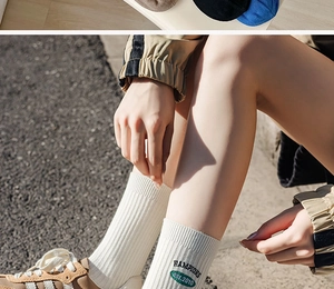 Detailed close-up of white crew socks featuring green letter embroidery and cotton texture