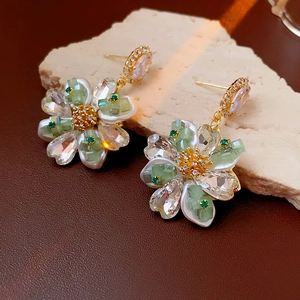 Détail de boucles d'oreilles fleuries vert pastel avec plaqué or sur pierre texturée
