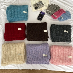 Flat lay of colorful wool knit scarves and gloves set on white cozy bedding fabric
