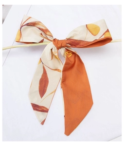 Detail of a satin scarf tied on a branch featuring orange and cream leaf prints