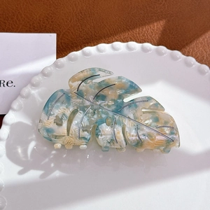 Detailed macro view of acetate monstera leaf hair claw with blue marble texture on ceramic tray