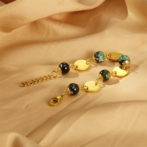 Detail view of gold circular discs and dark green resin beads on a steel chain