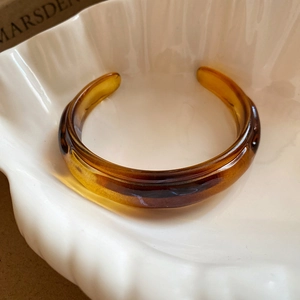 Close-up of amber resin cuff bracelet with tortoiseshell texture in a white shell dish