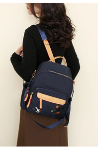 Detail of navy nylon backpack featuring rabbit embroidery and leather accents on model