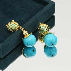 Elegant turquoise drop earrings with gold woven frames on a green velvet box