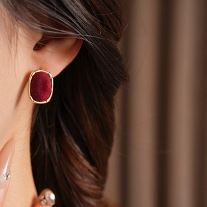 Close-up of a red velvet oval earring with gold trim worn on a model's ear