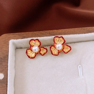 Macro shot of 18k gold flower earrings with red enamel and white pearls in a jewelry box