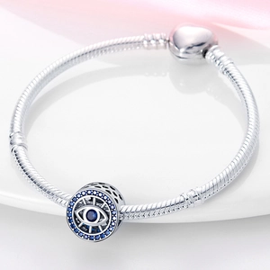 Macro detail of silver snake chain bracelet with blue evil eye bead on soft fabric