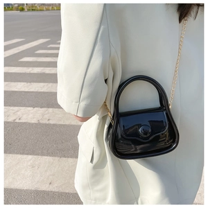 Close-up of a glossy black mini jelly bag with a gold chain strap on a street background
