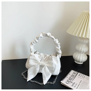 Close-up of white bow-knot cloud handbag with metal chain and pleated handle on table