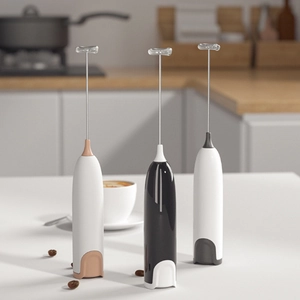 Handheld electric milk frother in three colors on a white table with coffee beans