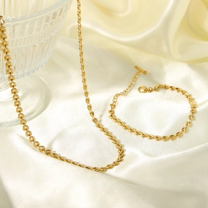 Golden heart-shaped stainless steel necklace and bracelet set on soft silk fabric