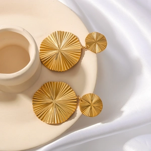 Golden double disc earrings with fan pleated sunburst texture on cream ceramic tray