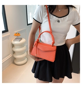Detail of orange handbag showing wavy embossed texture and stylish knotted handle