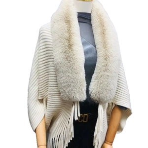Elegant cream knit poncho cape featuring a lush faux fur collar and decorative fringe trim