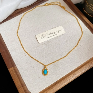 Detail of vintage gold necklace with turquoise oval pendant on a rustic wood tray