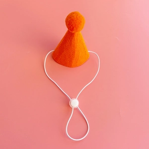 Close-up of orange pet birthday hat with pom-pom and adjustable white elastic strap