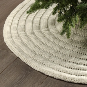 Detail of cream white cable knit Christmas tree skirt on rustic dark wood floor texture