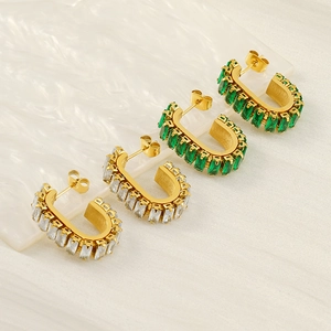 U-shaped gold earrings set with rectangular clear and green zircon stones on white texture