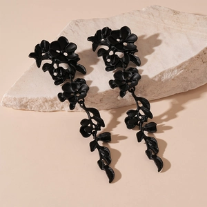 Close-up of matte black flower tassel earrings on stone decor with soft side lighting