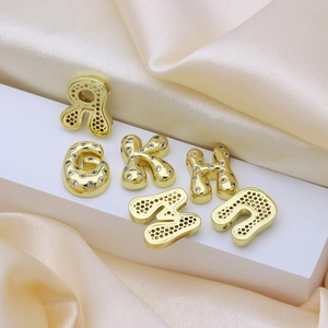 Golden balloon style letter pendants with sparkling zirconia set on a white pedestal