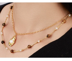 Close-up of double-layer gold necklace with tiger eye stone and white pearl detail