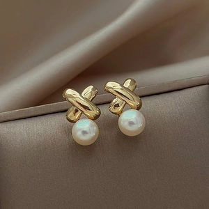 Macro shot of gold cross-shaped earrings with round pearls on luxury silk fabric