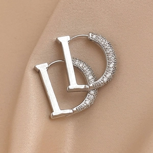 Close-up of interlocking metal letter D earrings with sparkling zircons on champagne silk