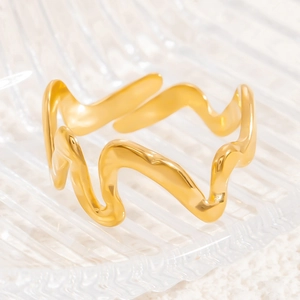 Close-up of gold wave ring with smooth minimalist curves on glass over white fabric