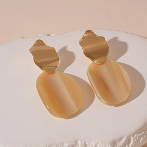 Détail de boucles d'oreilles ovales en résine beige et métal doré sur socle en pierre