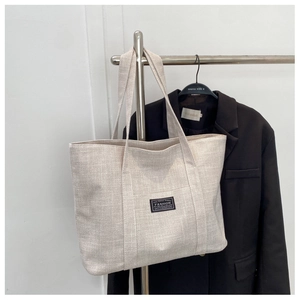 Detailed close-up of oatmeal canvas tote bag texture with fashion label and long straps