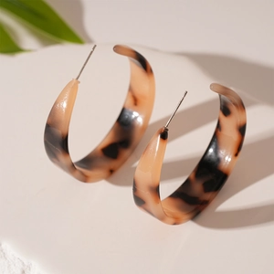 Vue macro de boucles d'oreilles créoles en résine à motif léopard avec clous en argent