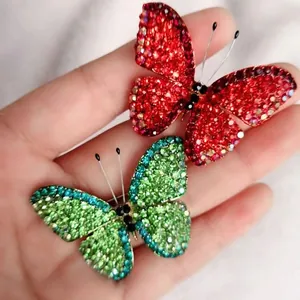 Close-up of vibrant red and green butterfly brooches with shimmering rhinestones in hand