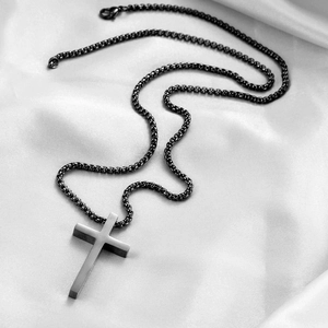 Détail d'un pendentif croix en acier noir sur un élégant fond en soie blanche soyeuse