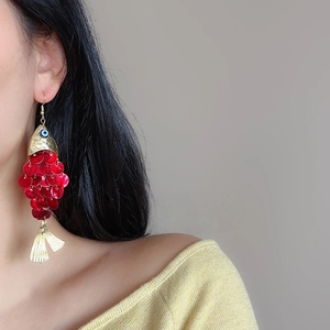 Detail shot of long red sequined fish dangle earrings on a model with golden finish