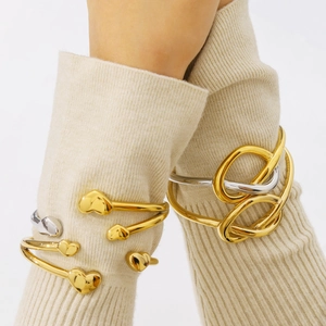 Polished 18k gold heart and knot minimalist open bangles worn over a beige sweater