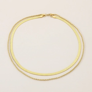 Vue détaillée du collier double couche doré avec chaîne serpent et cordelette sur beige