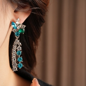 Close-up of elegant silver-tone drop earrings with blue and green crystals on model