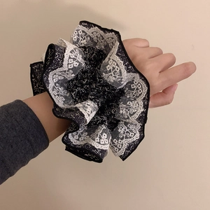 Détail d'un chouchou floral avec dentelle porté au poignet sur fond beige doux