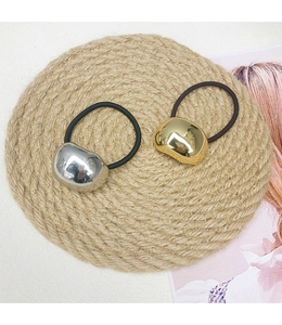 Detail of minimalist metallic pebble hair ties in gold and silver on a textured mat