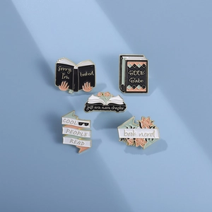 Five enamel book pins with reading quotes on a blue background in natural light