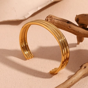 Three-layer open stainless steel bangle in 18K gold finish on a natural wood stand