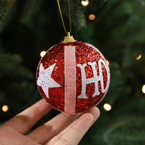 Sparkly red Christmas ball ornament with HO lettering held against a festive tree background
